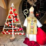 Rzeczywistej wielkości postać świętego Mikołaja ubranego w albę, ornat i mitrę, z pastorałem i workiem z prezentami w rękach. Obok sylwetka choinki na, której pozawieszane są papierowe serduszka